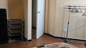 Una habitación con un alfombrado estampado, una lámpara en el techo, un perchero y una puerta que da a otra estancia.