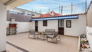 Een terras met een barbecue, twee stoelen en een tafel met een fles en druiven.