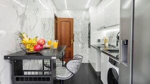 Een compacte keuken met een marmeren spatwand, een houten deur, een eettafel met stoelen en een wasmachine.