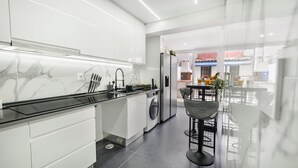 Een moderne keuken met witte kasten, een zwart aanrecht en een achterwand van marmer. Een eethoek met een tafel en stoelen is zichtbaar door een glazen scheiding.