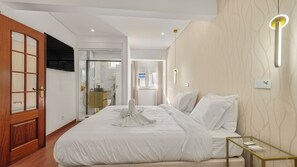 A modern hotel room with a large bed, a bedside table, a bathroom with a glass door, and a view of the outside.