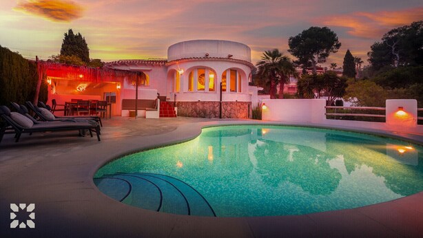 A pool area with lounge chairs, a building with arched windows, and a sunset sky. - Villa BUENA VIDA by Abahana Villas (Javea / Xàbia)