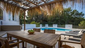 A wooden table with a bowl of fruit, outdoor seating, and a pool in the background. - Villa BUENA VIDA by Abahana Villas (Javea / Xàbia)