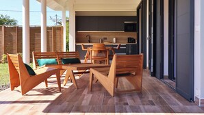 Un espacio de comedor al aire libre techado, con mobiliario de madera y vista a una cocina moderna.