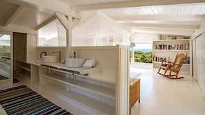 A modern, open-plan living space with a large window overlooking a scenic view, a built-in bookshelf, and a cozy reading chair. - Villa Blanche with magnificent sea views and infinity pool at your disposal (Grand-Bourg)