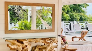 A room with a glass-top table featuring a natural wood design, a white chair, and a view of a white fence and greenery outside. - Villa Blanche with magnificent sea views and infinity pool at your disposal (Grand-Bourg)