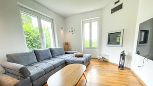 En moderne stue med en grå hjørnesofa, et træsofabord og et fladskærms TV monteret på væggen.
