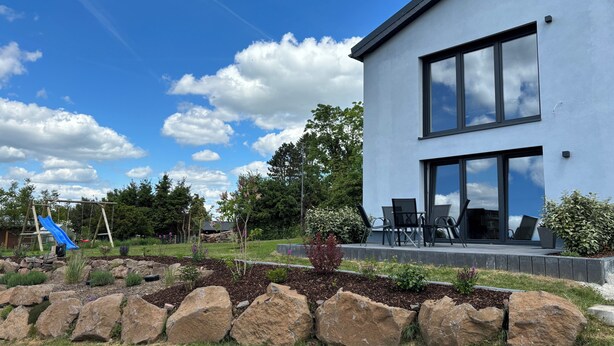 Ein modernes, zweistöckiges Haus mit Terrasse und Sitzgelegenheit im Freien.