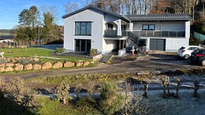 Ein modernes, zweigeschossiges Haus mit großem Balkon, Garage und Auffahrt.