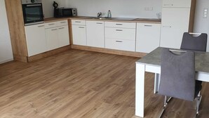 Eine moderne Küche mit weißen Schränken, einer Holzauskładung und einem Essbereich mit Tisch und Stuhl.