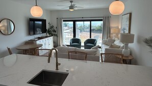 Een moderne keuken met een groot kookeiland, een eethoek met stoelen, een bank en een aan de muur bevestigde televisie.