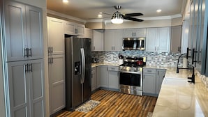 A modern kitchen with grey cabinets, stainless steel appliances, a wooden floor, and a ceiling fan. - Charming 3-bedroom Lake Cottage with Dock, WiFi, & AC on enjoyable Houghton Lake (Houghton Lake)
