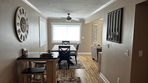 A dining area with a wooden table, chairs, a ceiling fan, and a large window. - Charming 3-bedroom Lake Cottage with Dock, WiFi, & AC on enjoyable Houghton Lake (Houghton Lake)