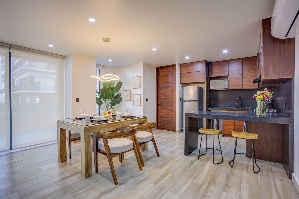 Una cocina moderna con armarios de madera, una isla central con taburetes y una mesa de comedor con sillas.