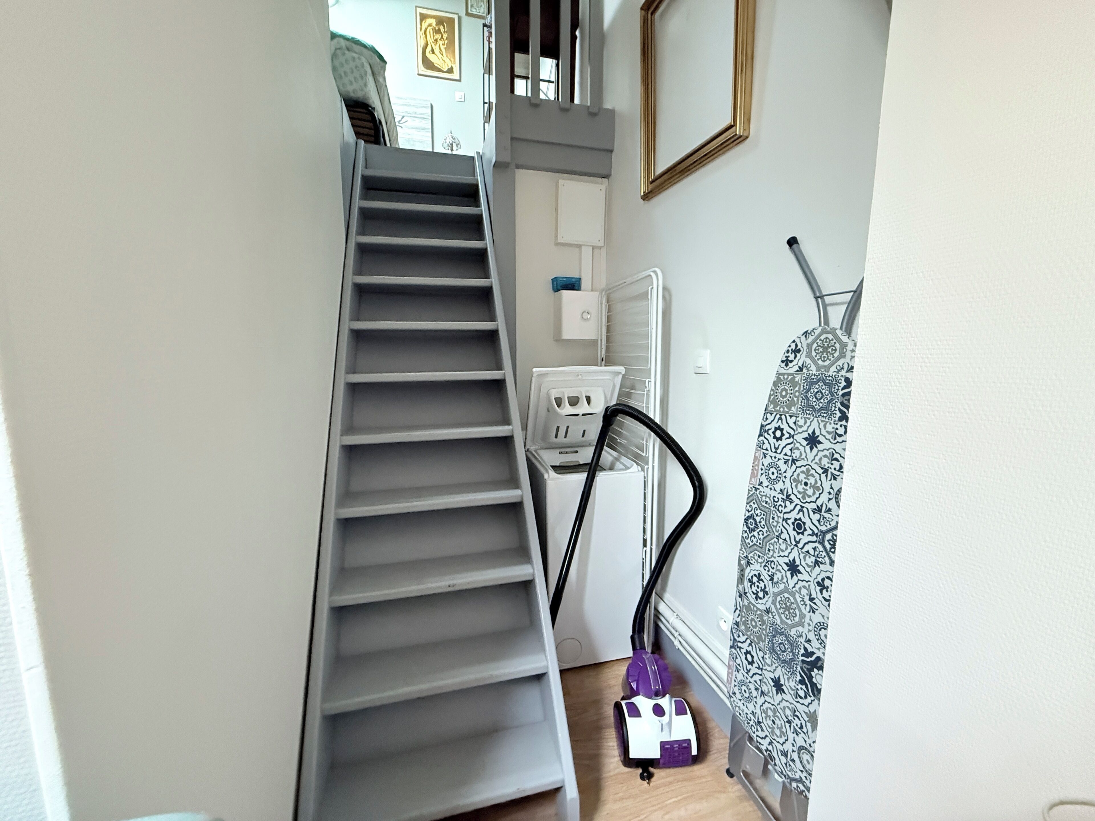 A staircase leading to a landing with a vacuum cleaner and laundry basket on the floor.