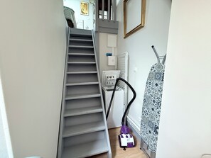 A staircase leading to a landing with a vacuum cleaner and laundry basket on the floor.