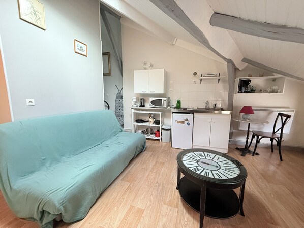A compact living space with a sofa, a small table with a clock, a kitchenette, and a chair.