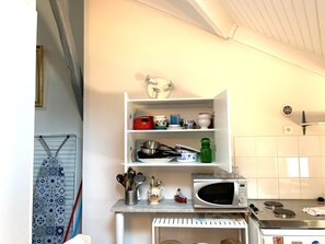 A kitchen with a microwave, stove, and various kitchen utensils on shelves.