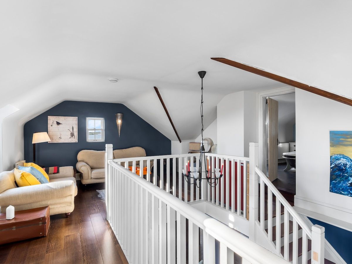 Un espace de vie de style industriel, avec un plafond haut, une rambarde blanche et un escalier menant à un niveau supérieur.