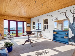 A room with a wooden ceiling, large windows, a dining table, a blue cabinet, and a view of the outdoors. - Suantraí Cottage (Cashel)