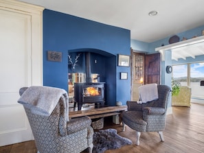 A room with a blue wall, a fireplace, two patterned armchairs, and a wooden bench. - Suantraí Cottage (Cashel)