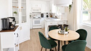 A modern kitchen with white cabinets, a central island, and a dining area with green chairs.