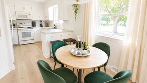 A modern kitchen with white cabinets, a central island, and a dining area with green chairs.