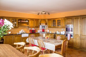 A kitchen with wooden cabinets, a dining table with chairs, a microwave, an oven, and a chandelier.