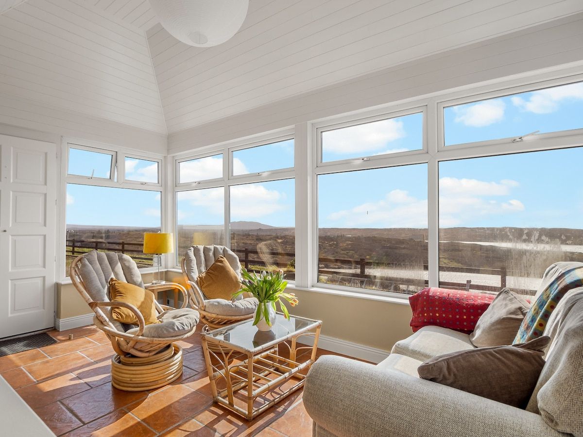 A room with a large window, wicker furniture, and a view of the landscape.