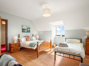 A bedroom with two beds, wooden flooring, a skylight, and a painting on the wall.