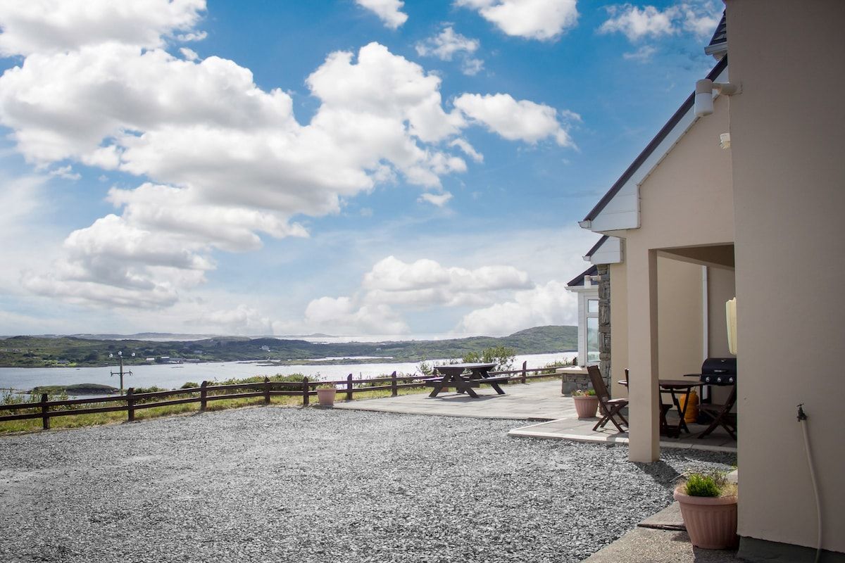 Un espace patio offrant une vue sur un lac et des collines, avec une table de pique-nique et des sièges d’extérieur.