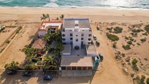 Un hotel frente a la playa con varias construcciones, una zona de estacionamiento y vistas a la playa.