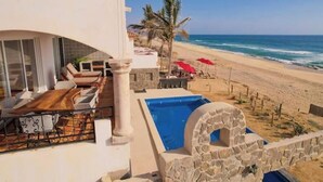 Zona de piscina con vista a la playa, mobiliario exterior y una estructura de piedra.