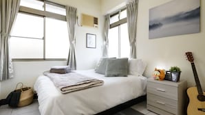 Un dormitorio con cama, una guitarra, una mesita de noche y una ventana con cortinas.