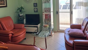 Una sala de estar con dos sofás de cuero rojo, una mesa de centro de vidrio, un televisor, un aparador decorativo de vidrio y una araña.
