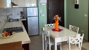 Una cocina compacta con armarios blancos, un refrigerador de acero inoxidable y una zona de comedor con una mesa y sillas blancas.