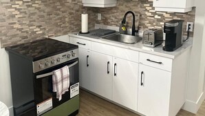 Une cuisine moderne avec des armoires blanches, un four à micro-ondes encastré, une cuisinière, un évier et une machine à café.