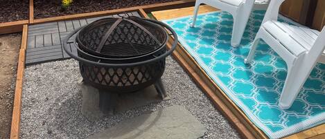A backyard with a fire pit, two white Adirondack chairs, a blue patterned rug, and a wooden fence.