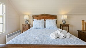 A bedroom with a wooden headboard, two bedside tables with lamps, a bed with a floral-patterned bedspread, and rolled towels on the bed. - Apollo Bay Guesthouse (Apollo Bay)