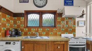 A kitchen with a washing machine, a stove, a sink, and a window with a view. - Apollo Bay Guesthouse (Apollo Bay)