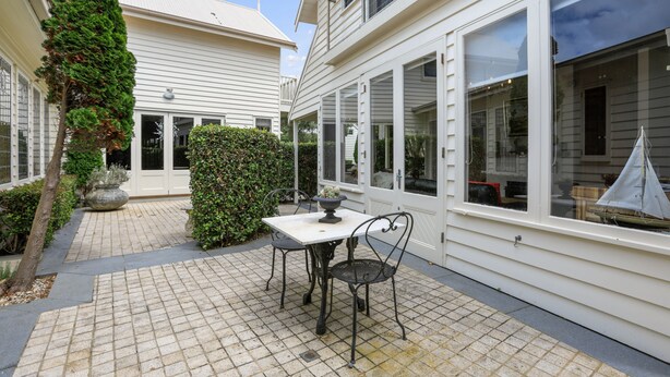 A courtyard with a tiled floor, a table with chairs, and a hedge. - Apollo Bay Guesthouse (Apollo Bay)