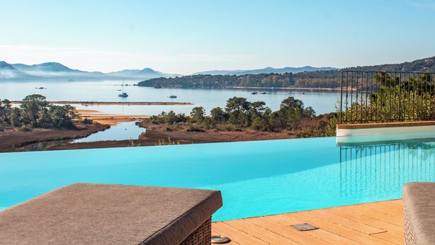 A clear view of a swimming pool with a wooden deck and lounge chairs, overlooking a calm lake with boats and distant hills. - Villa Golfo Di Sogno (porto vecchio)