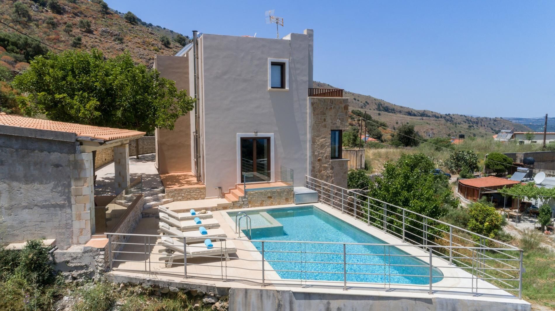 A modern villa with a swimming pool, stone walls, and a view of the surrounding landscape.