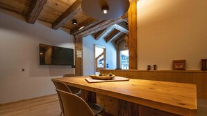 Ein Holztisch mit Stühlen, eine Obstschüssel und ein an der Wand befestigter Fernseher.