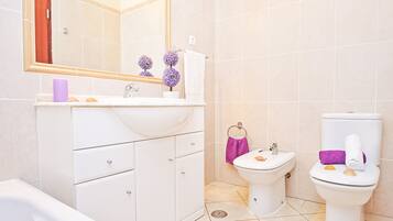 Ein Badezimmer mit weißem Waschbecken, Spiegel, Waschtisch, Toilette und Badewanne.