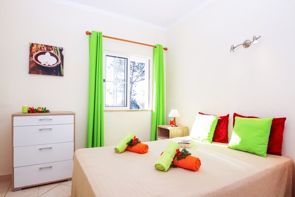 A hotel room with a bed, a bedside table with a lamp, a dresser, and a window with curtains.