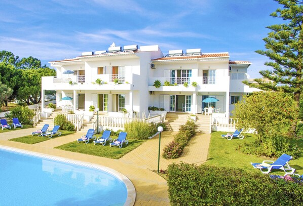 A two-story hotel with a swimming pool, sun loungers, and a well-maintained garden.