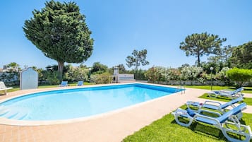 Una piscina con sillas de descanso, un área de barbacoa y un gran árbol.