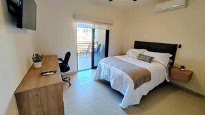 Une chambre à coucher comprenant un lit, un bureau, une chaise, un ventilateur de plafond et un téléviseur fixé au mur.