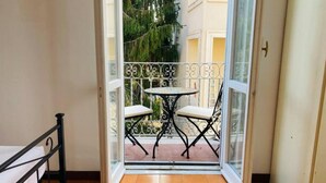 A balcony with a table and two chairs, a bed, and a door leading outside. - Cozy Apartment in the Heart of Rome- St. Peter's & Vatican (Roma)